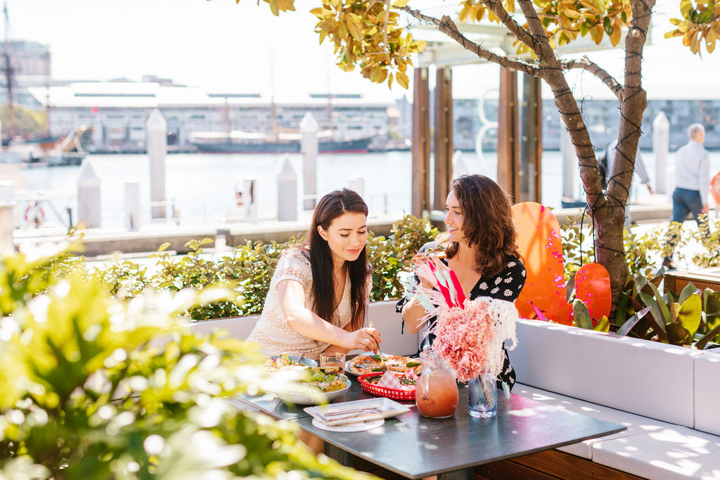 People dining outside with a harbour in the background.