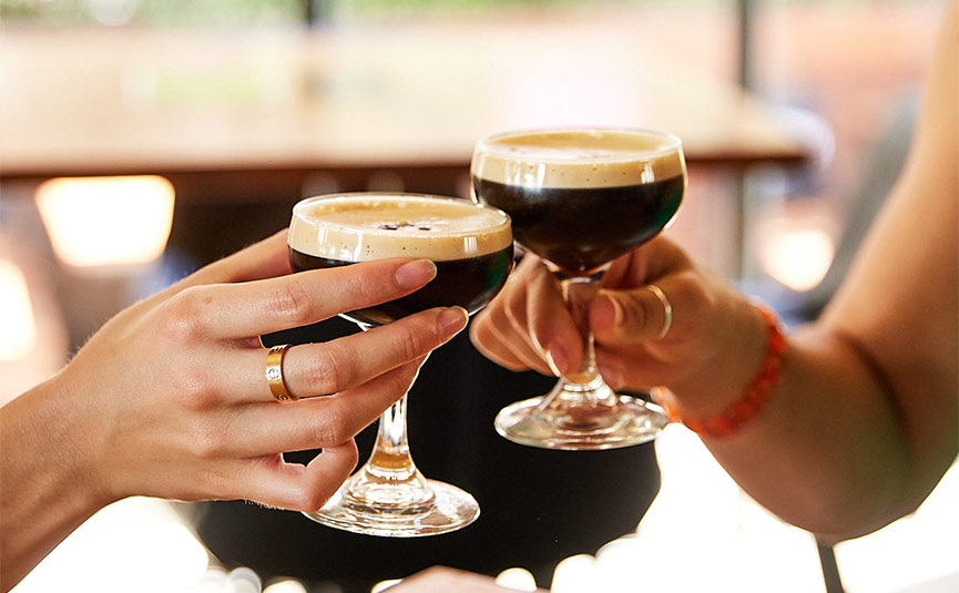 Two hands clinking Espresso martini cocktails at a bar