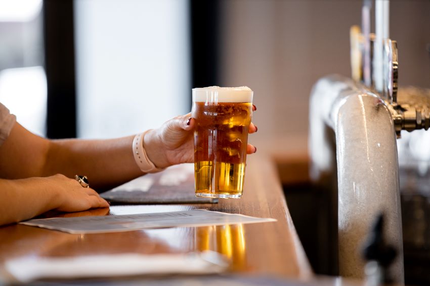 A hand holding two beer glasses at a bar