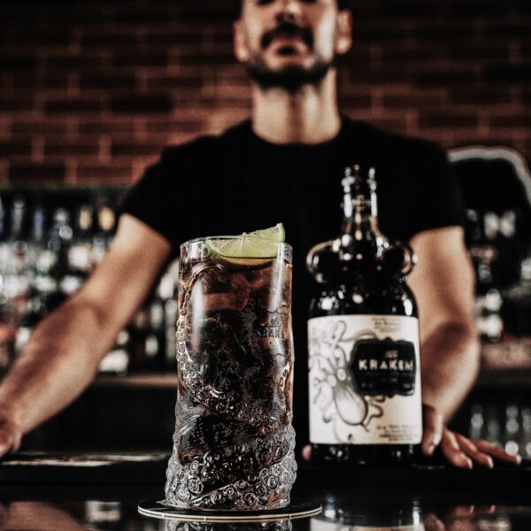A bottle of Kraken Black Spiced Rum and a cocktail on a bar
