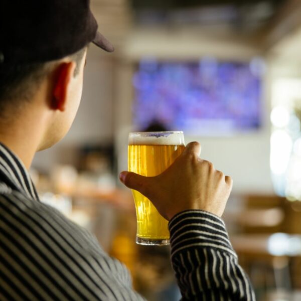 A punter holding a beer and watching sport on the tv at a bar