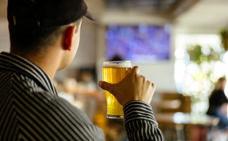 A punter holding a beer and watching sport on the tv at a bar